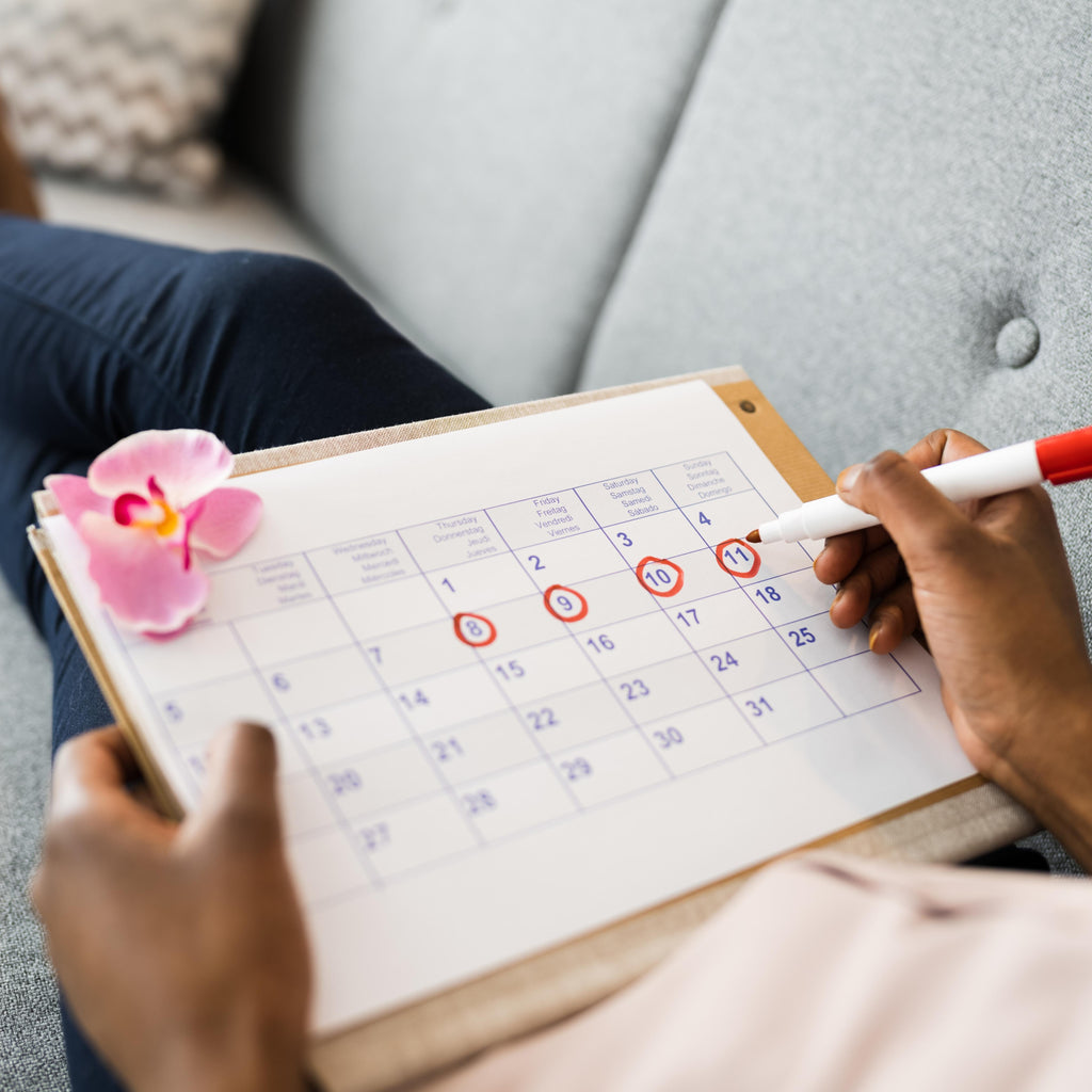 A woman relaxed on the couch, marking off her menstrual cycle days on her period-tracking calendar. 