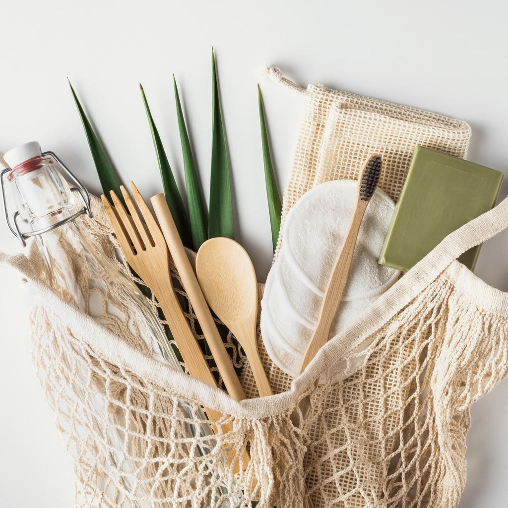 A reusable bag full of sustainable household essentials like bamboo cutlery and a glass water bottle